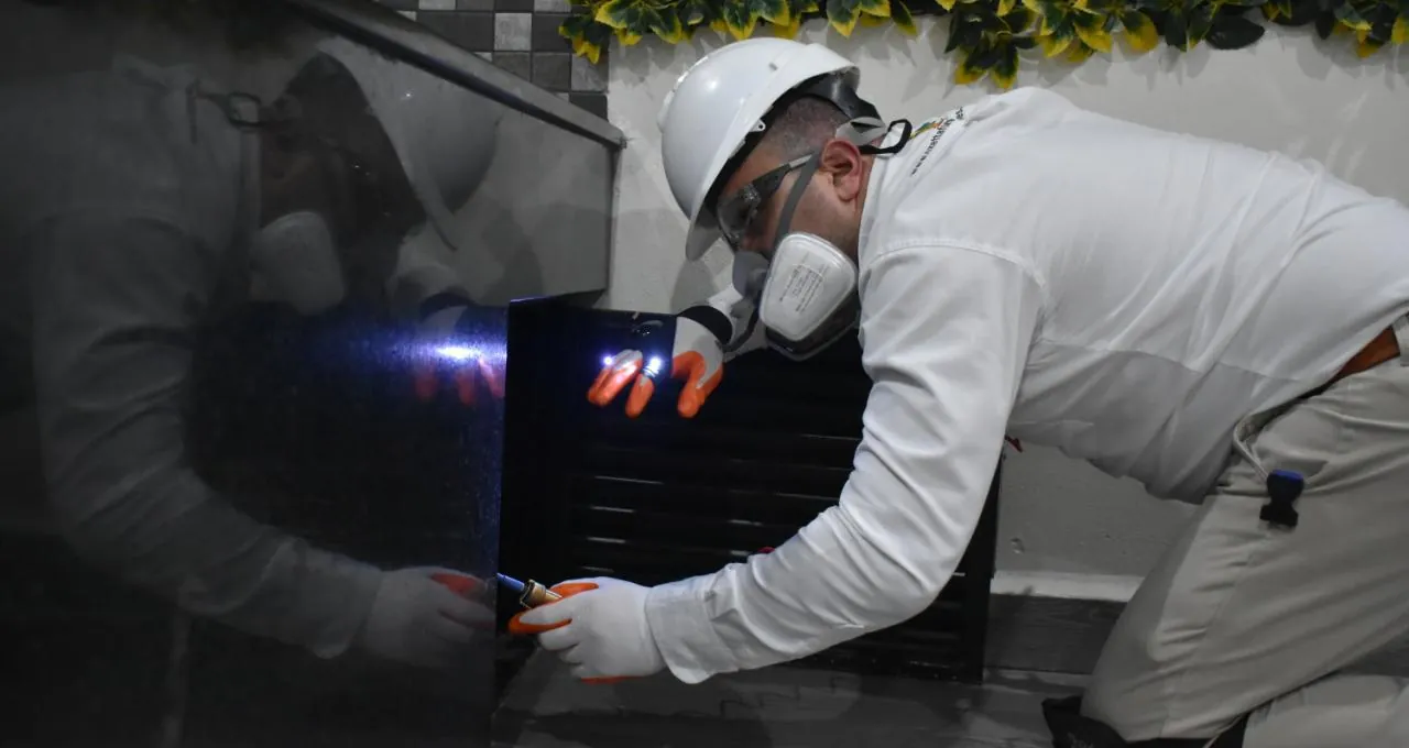 Técnico de Ozetta con lámpara revisando una rejilla a ras de piso durante una inspección contra alacranes en León