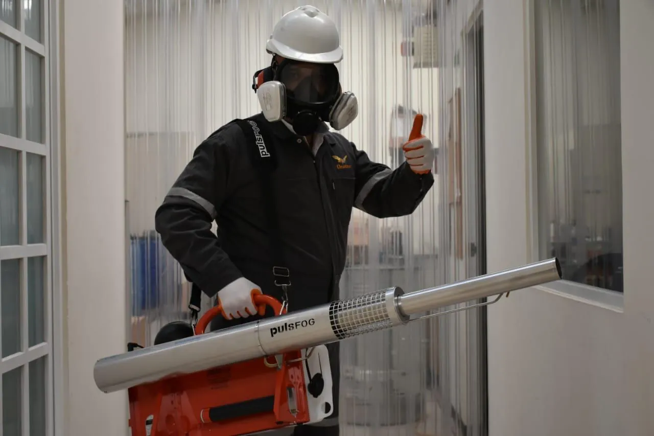 Técnico de Ozetta con equipo de protección y termonebulizador en un pasillo interior